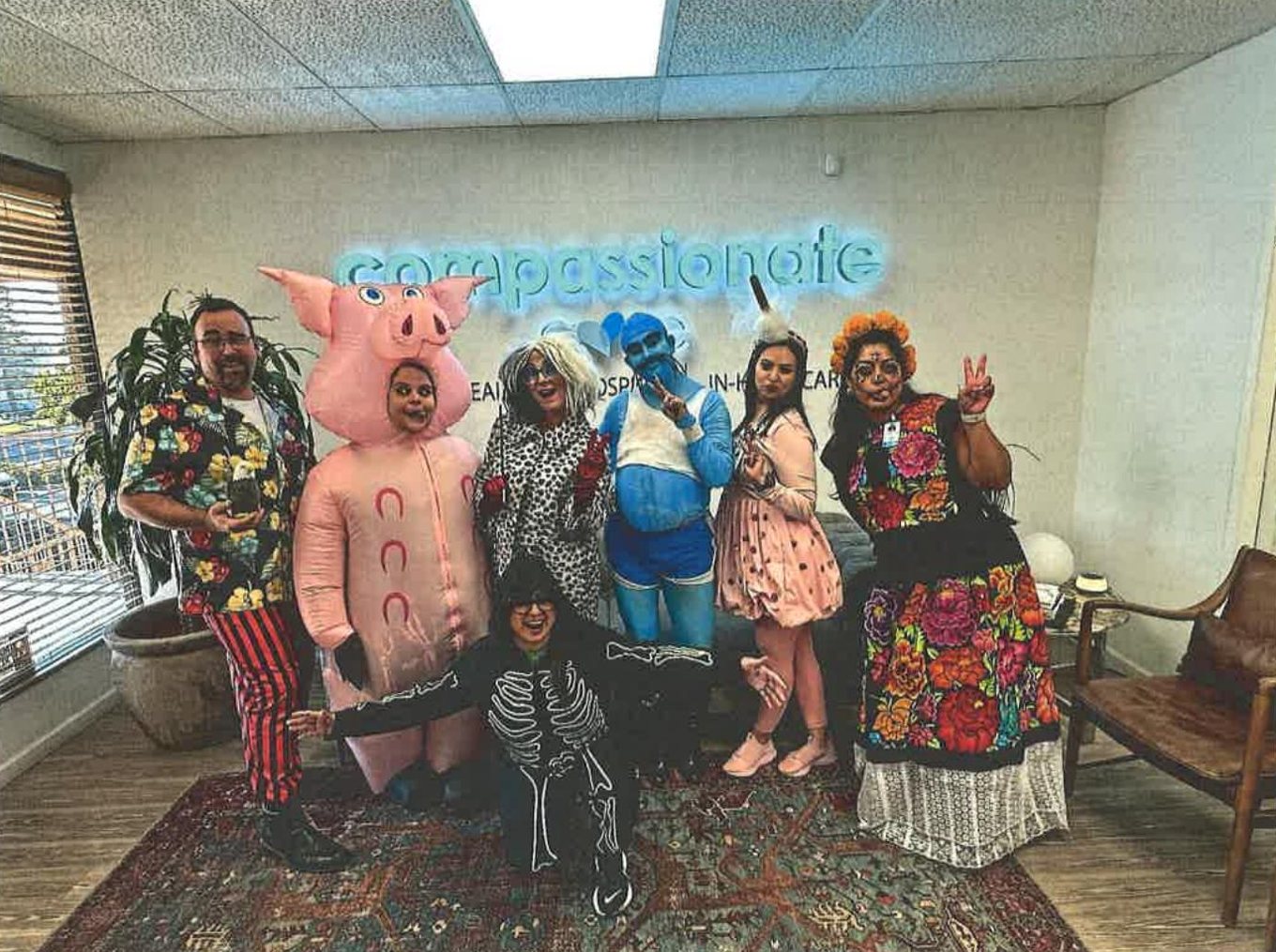 Fresno Hospice team in costume in front of the glowing Compassionate Care sign, 2025